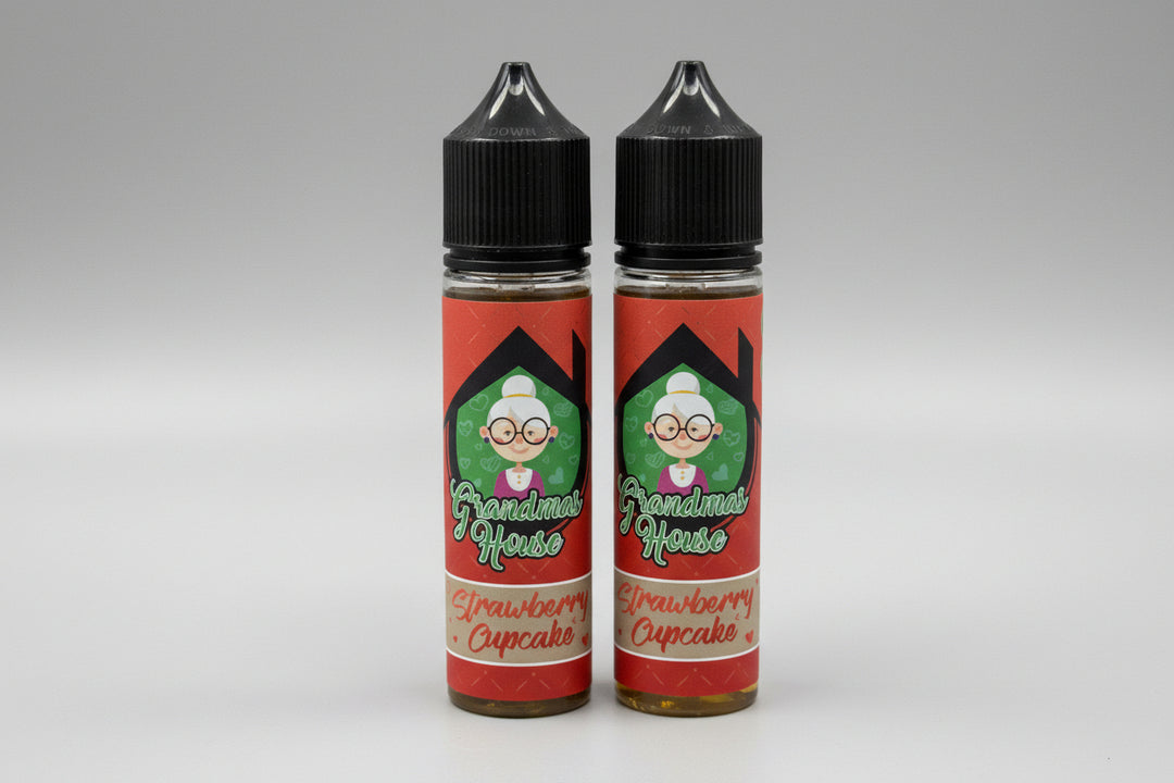 Two bottles of 'Grandma's House' Strawberry Cupcake-flavored e-liquid on a stone surface.